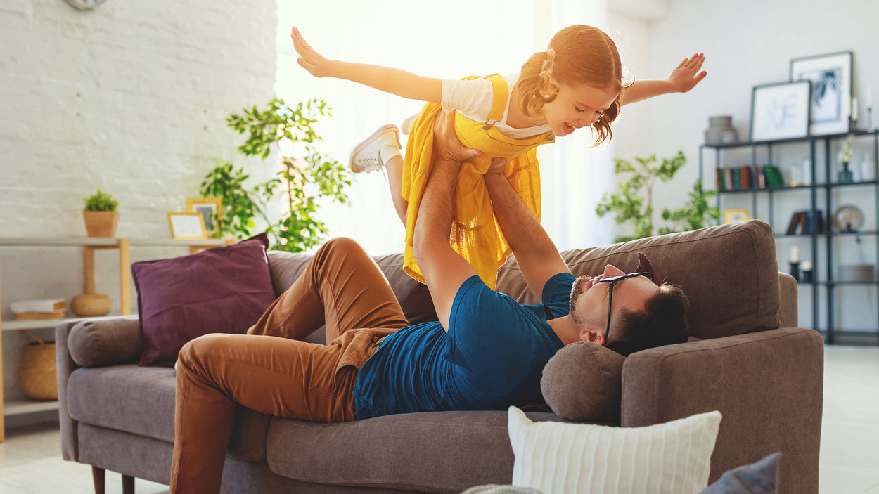 Father holding his daughter in the air while laying on the sofa in the living room