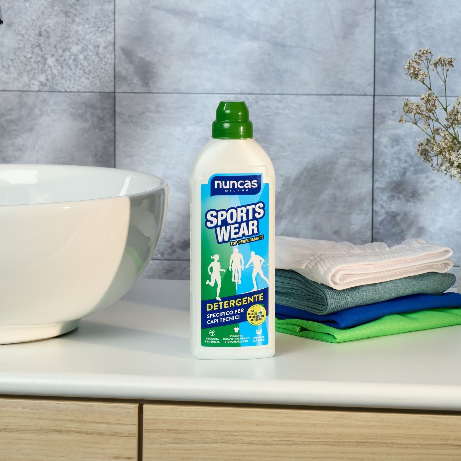SPortswear Detergente per capi tecnici Nuncas - Immagine ambientata del prodotto posizionato in un bagno vicino al lavandino vicino a capi sportivi