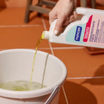 Winto Disincrostante forte per tutte le superfici resistenti agli acidi - 1000 ml viene versato in un secchiello per le pulizie. In sfondo un pavimento in cotto.