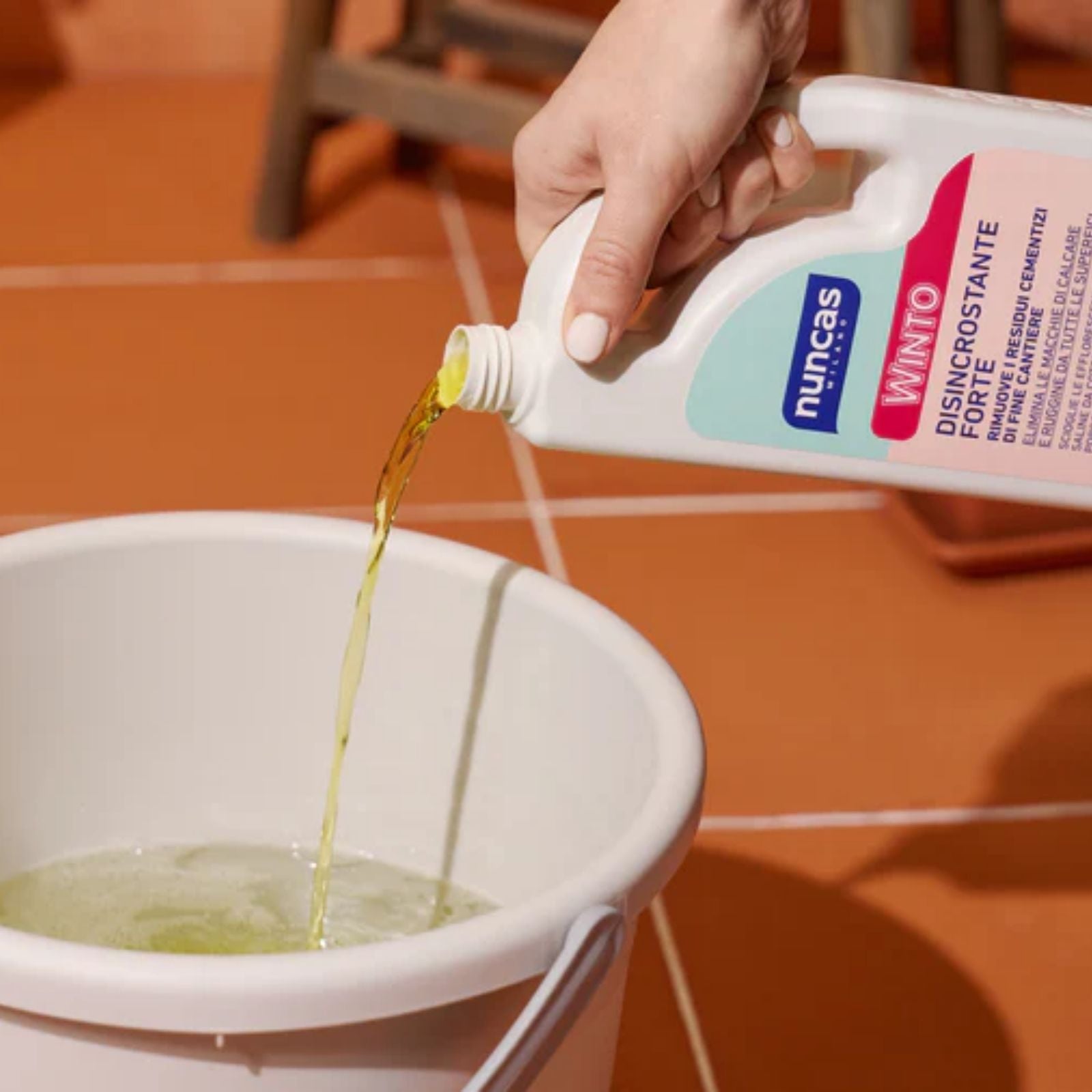 Winto Disincrostante forte per tutte le superfici resistenti agli acidi - 1000 ml viene versato in un secchiello per le pulizie. In sfondo un pavimento in cotto.