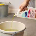Winto Disincrostante forte per tutte le superfici resistenti agli acidi - 1000 ml viene versato in un secchiello per le pulizie. In sfondo un pavimento in gres.