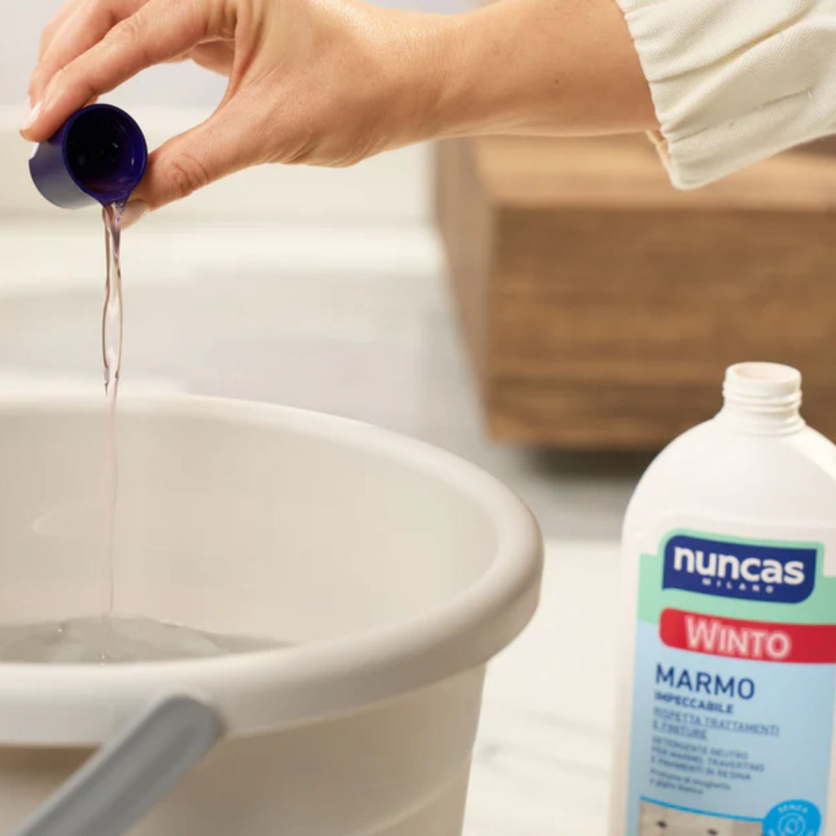 Un tappo di Winto Marmo Detergente neutro viene diluito in acqua all'interno di un secchio per le pulizie